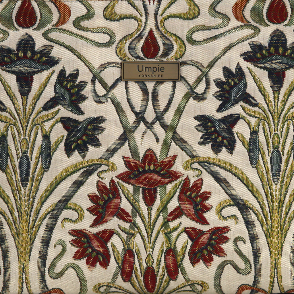 Close-up of Art Nouveau tapestry fabric on the Umpie Crossbody Bag — richly woven cream ground with deep burgundy irises, navy florals, and sage stems, with Umpie Yorkshire brand badge, by Umpie Handbags