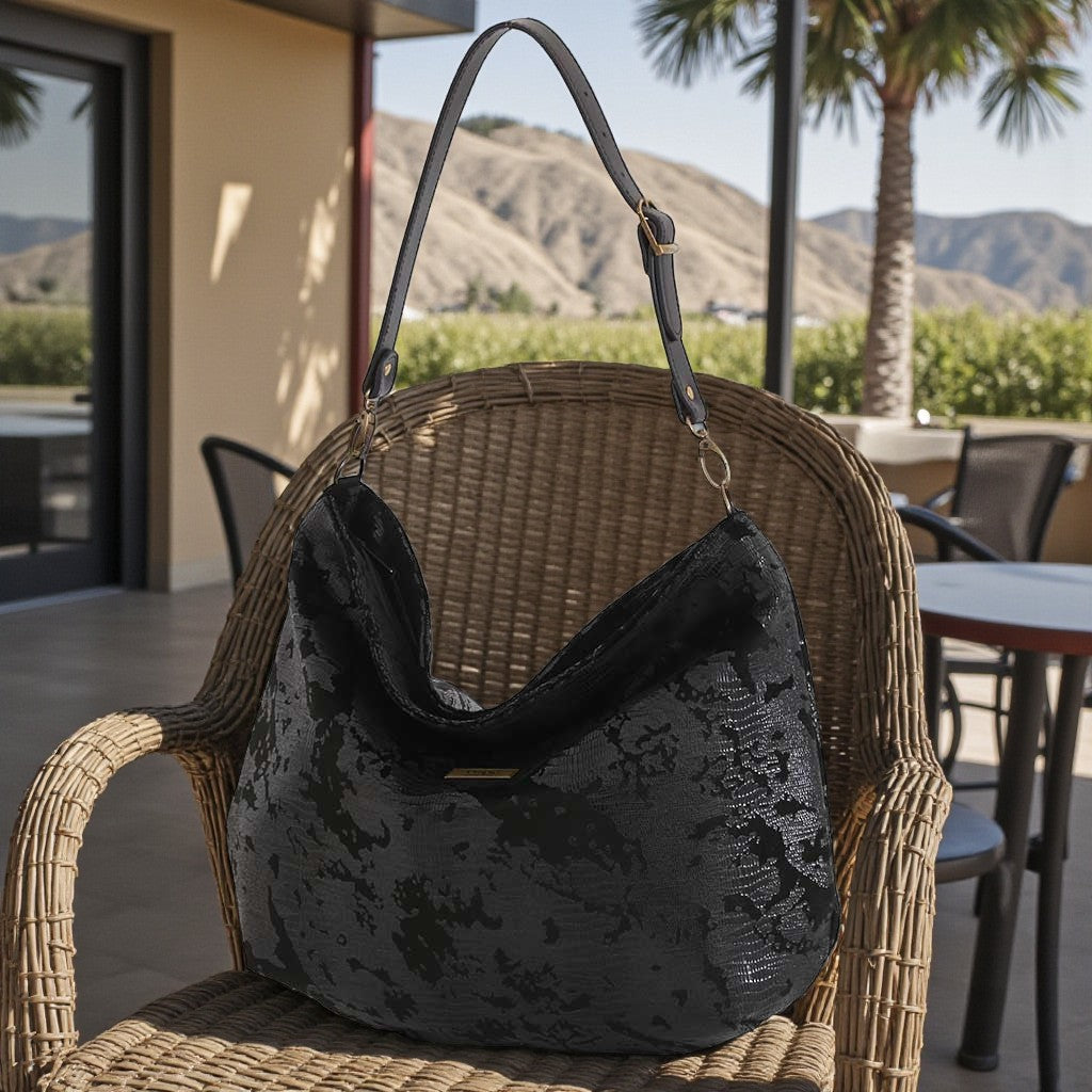 Black lizard print hobo bag side view showing zip top and adjustable leather strap detail, beachside terrace setting, by Umpie Handbags