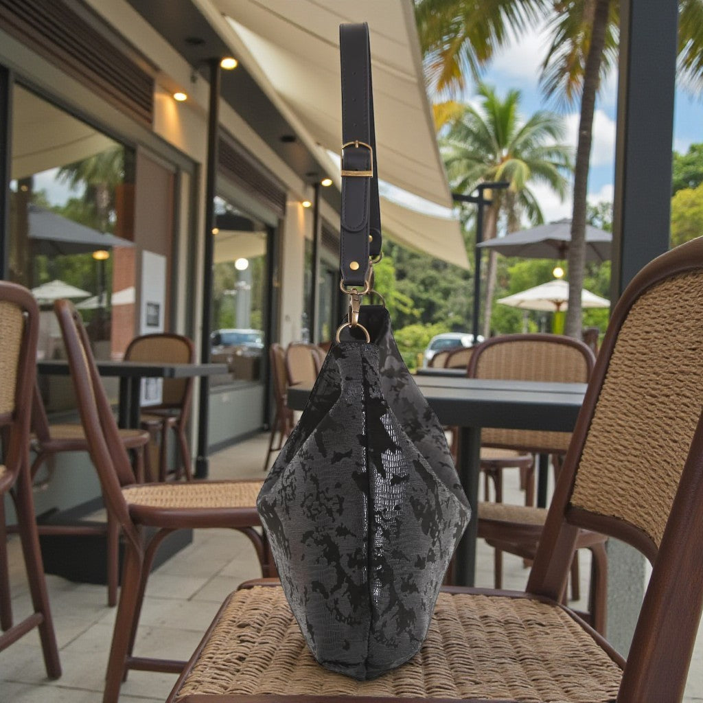 Black lizard print hobo bag standing upright on a wicker chair, showing black leather strap and gold clasp hardware, by Umpie Handbags