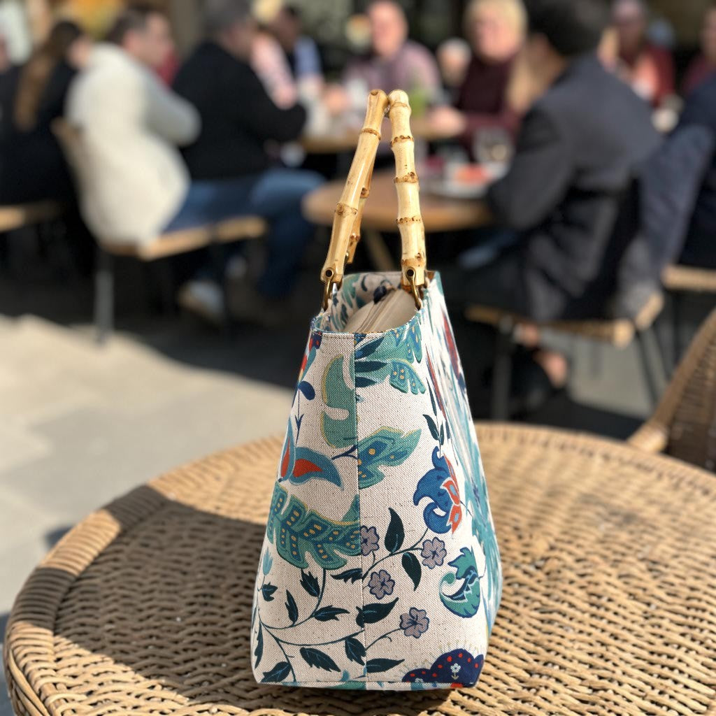 Side view of a floral linen handbag with bamboo handles on a table, highlighting the firm-backed structure that allows the bag to stand upright with quiet confidence, by Umpie Handbags