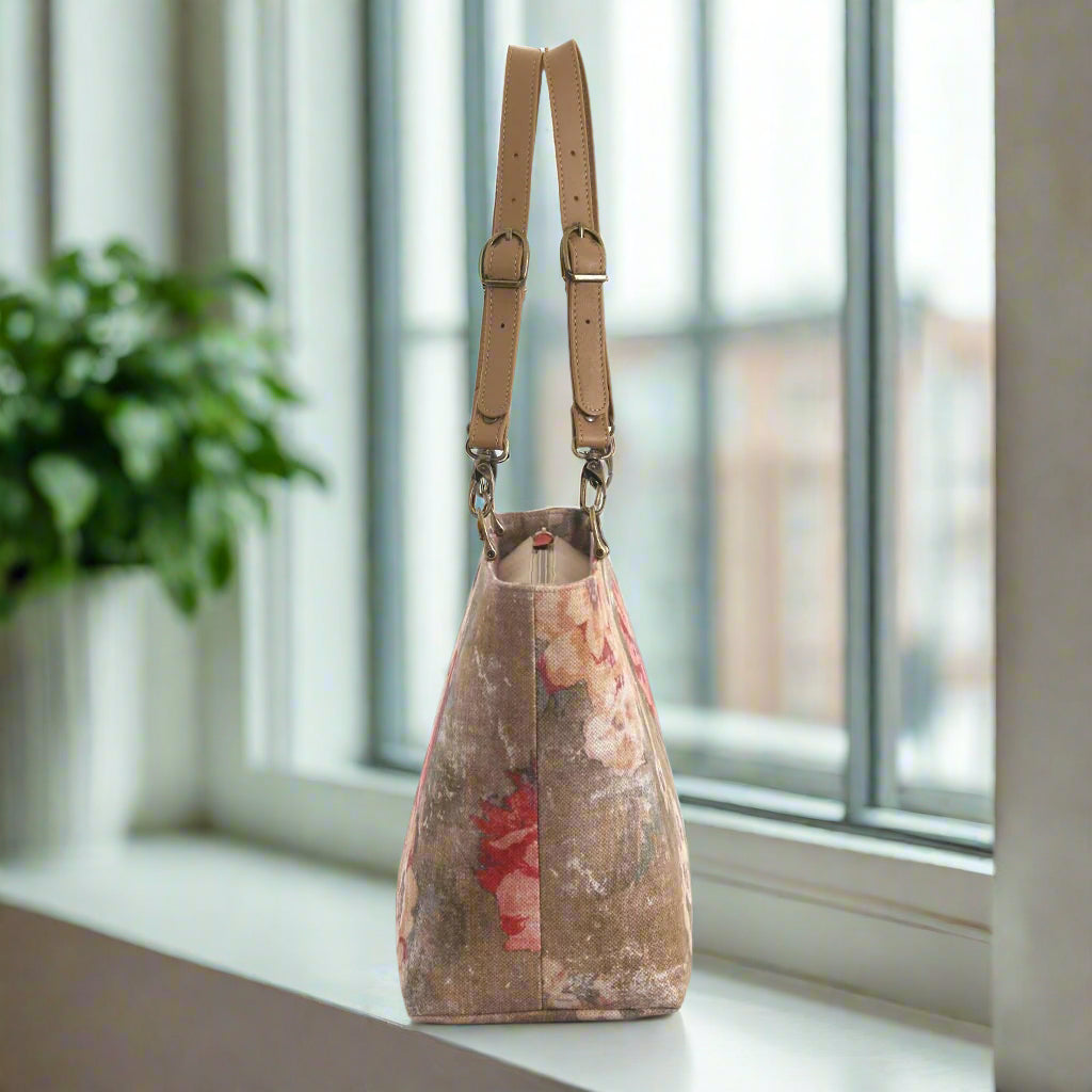 A side view of a shoulder bag in a beige and red  antique-style floral fabric with matching leather straps