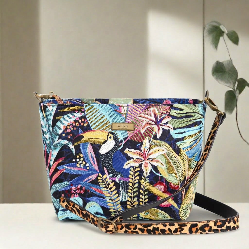 Full view of handcrafted floral crossbody bag featuring vibrant botanical print in greens and corals, adjustable leopard print leather strap, top-zip security, and sustainable British-made quality by Umpie Handbags