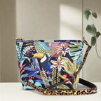 Full view of handcrafted floral crossbody bag featuring vibrant botanical print in greens and corals, adjustable leopard print leather strap, top-zip security, and sustainable British-made quality by Umpie Handbags