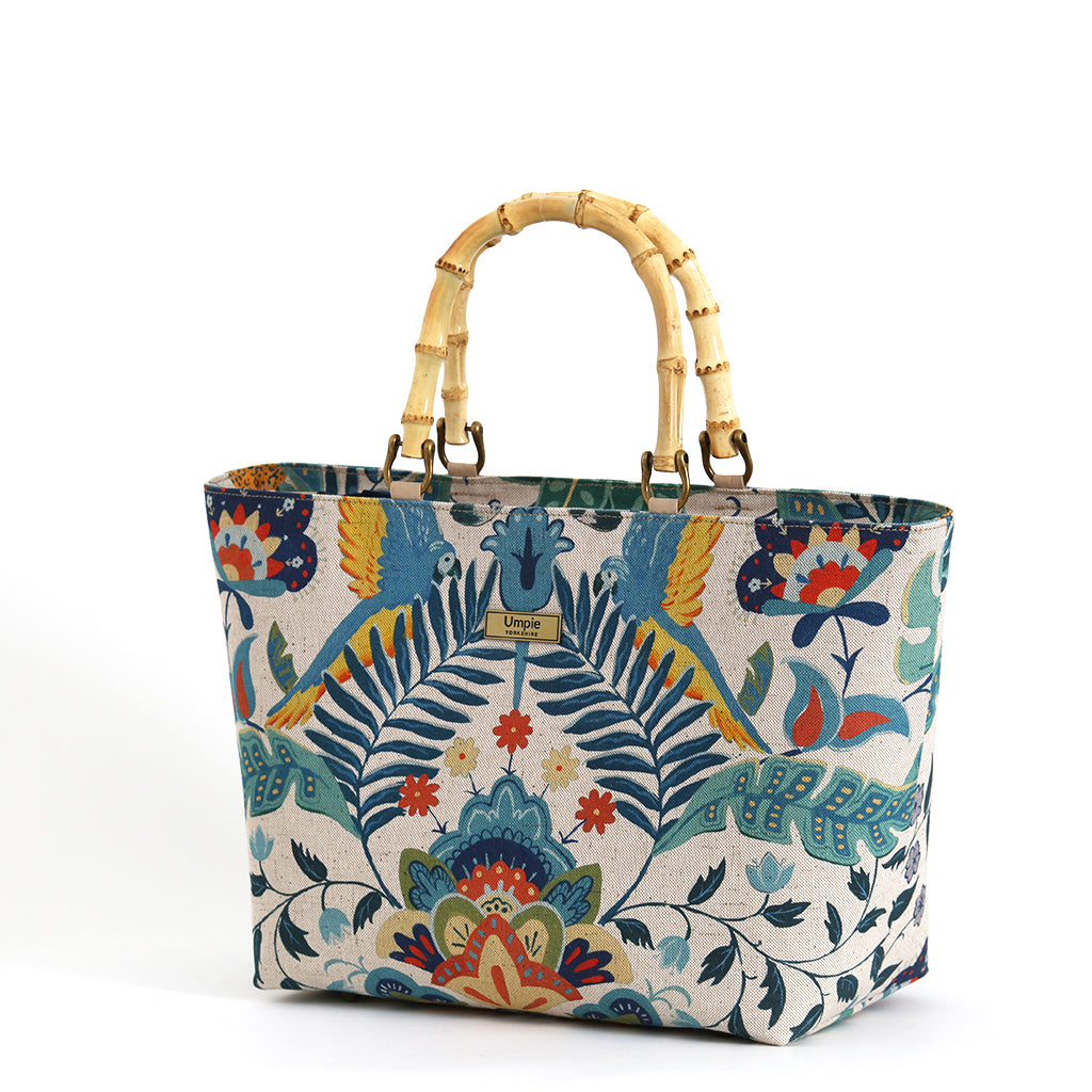 Front view of a floral linen handbag with bamboo handles standing upright showcasing the full botanical floral print and the warm natural curve of the bamboo handles, by Umpie Handbags