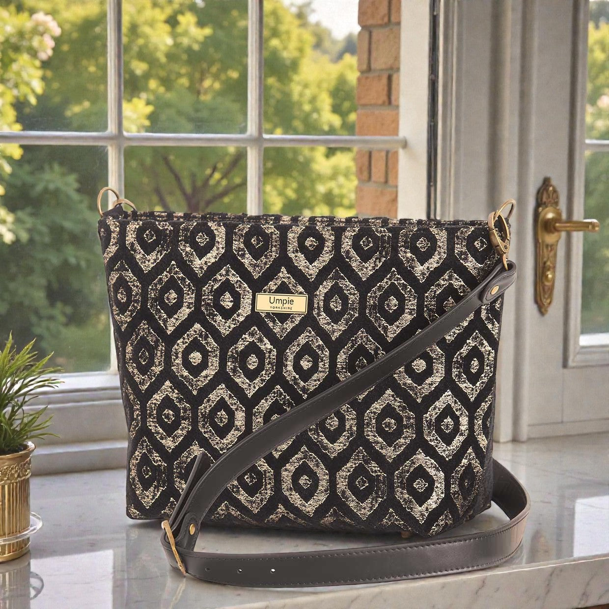 Gold metallic crossbody bag displayed at three-quarter angle, highlighting the premium black leather adjustable strap, fully lined interior with zip-top closure, and elegant proportions of handcrafted design by Umpie Handbags