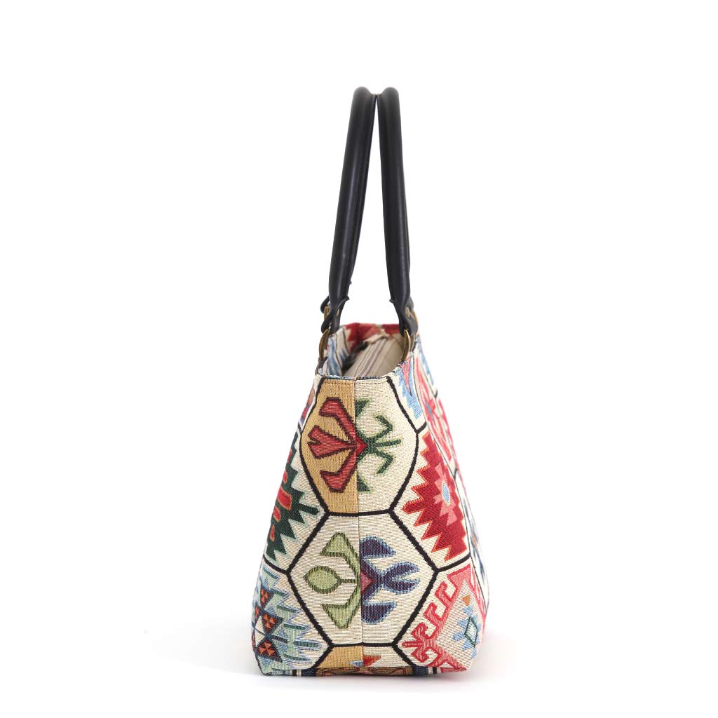 Side profile of the Hexagon Handbag showing the structured gusset and rich depth of the kilim-inspired tapestry fabric, with bold geometric hexagon panels in red, green and cream, black leather handles and antique brass hardware, by Umpie Handbags
