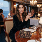 Leopard Print Cruise Clutch Bag sitting on a cruise ship dinner table beside a seated model dressed for the evening, bold leopard print leather with antique gold hardware, by Umpie Handbags