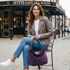 A woman seated on a street in York in front of Bettys tea rooms, carrying a purple velvet hobo bag with a leopard leather strap, by Umpie Handags