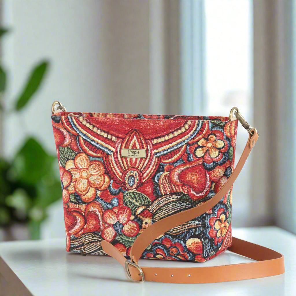 The Red Floral Crossbody Bag with a tan leather strap.