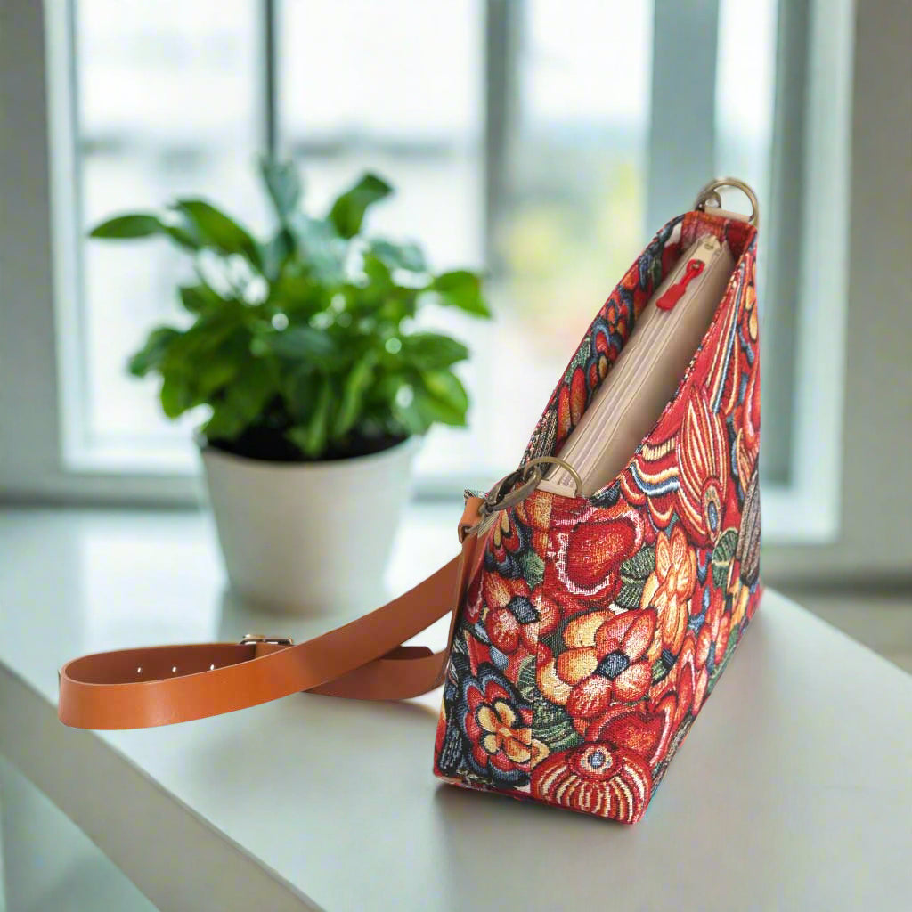 The Red Floral Crossbody Bag with a tan leather strap.