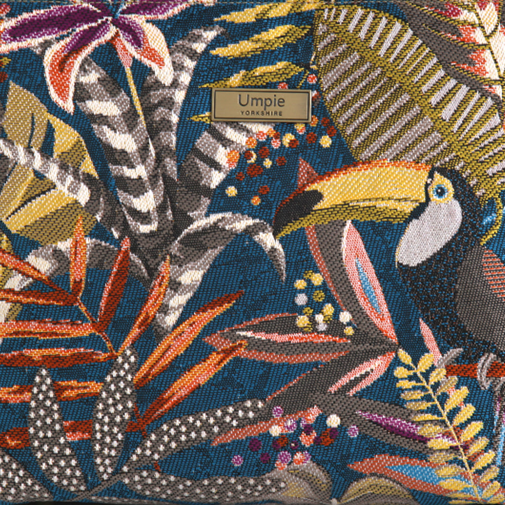 Close-up of toucan tapestry fabric showing exotic toucan with yellow beak, jewel-toned botanical foliage in burnt orange, gold and teal, richly woven texture, Umpie Yorkshire label, by Umpie Handbag