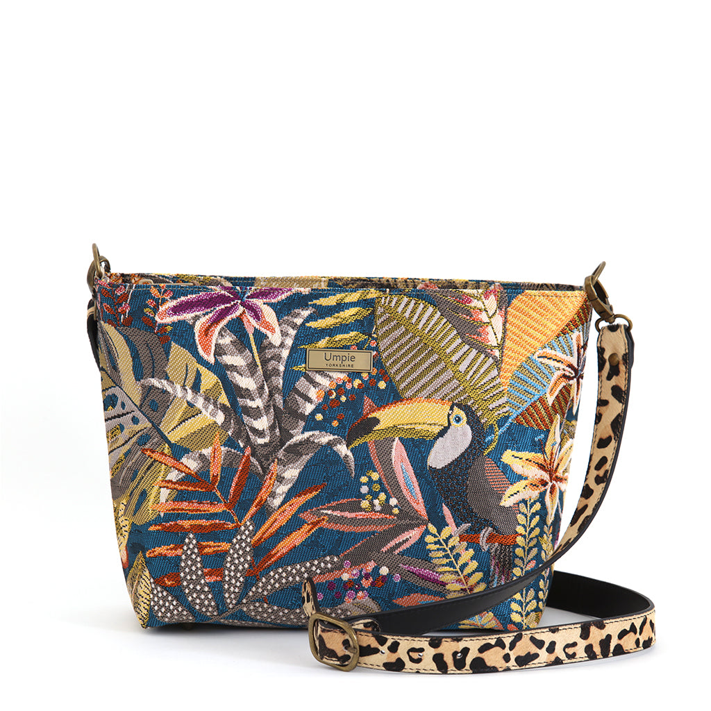 Toucan Tapestry Crossbody Bag on white background, full front view showing teal botanical tapestry fabric, toucan motif, leopard print leather strap and antique gold hardware, by Umpie Handbags