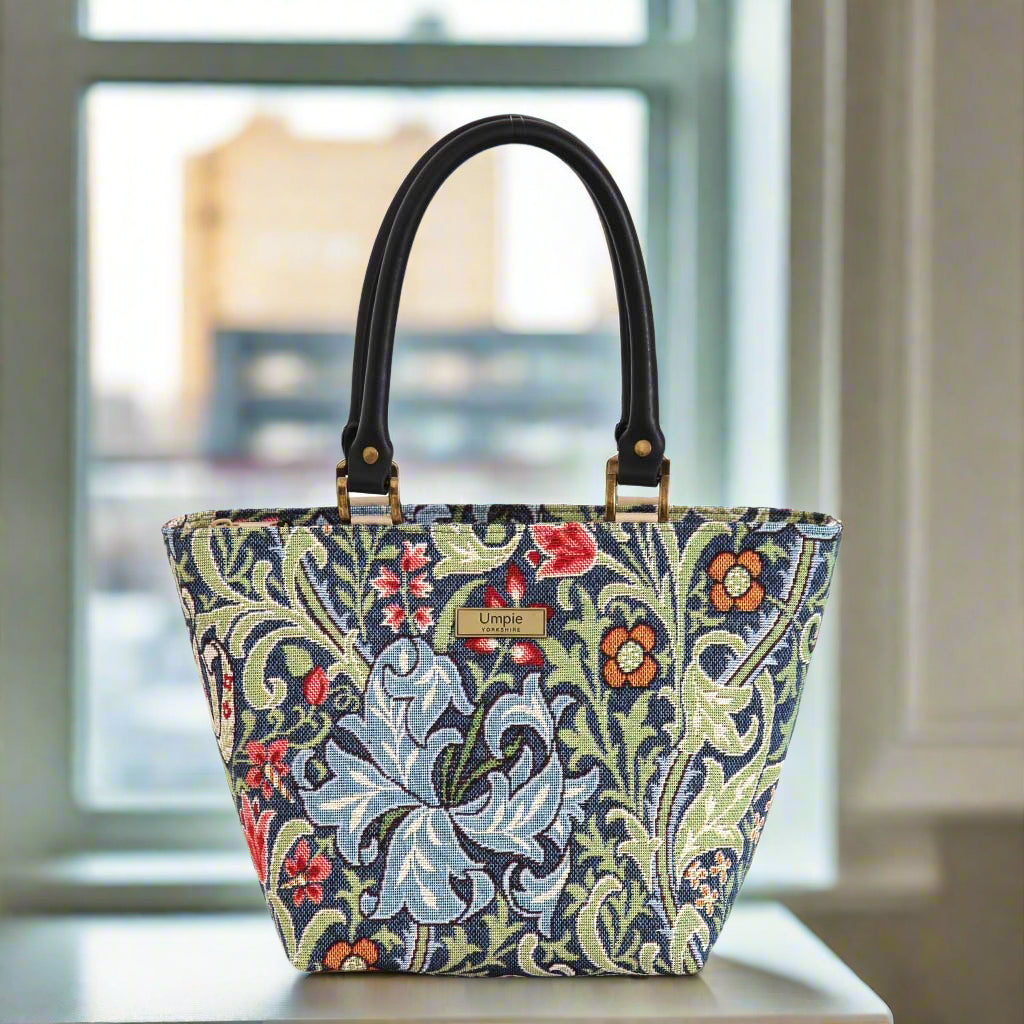 William Morris's floral-patterned handbag with black leather handles, on a surface with a blurred background