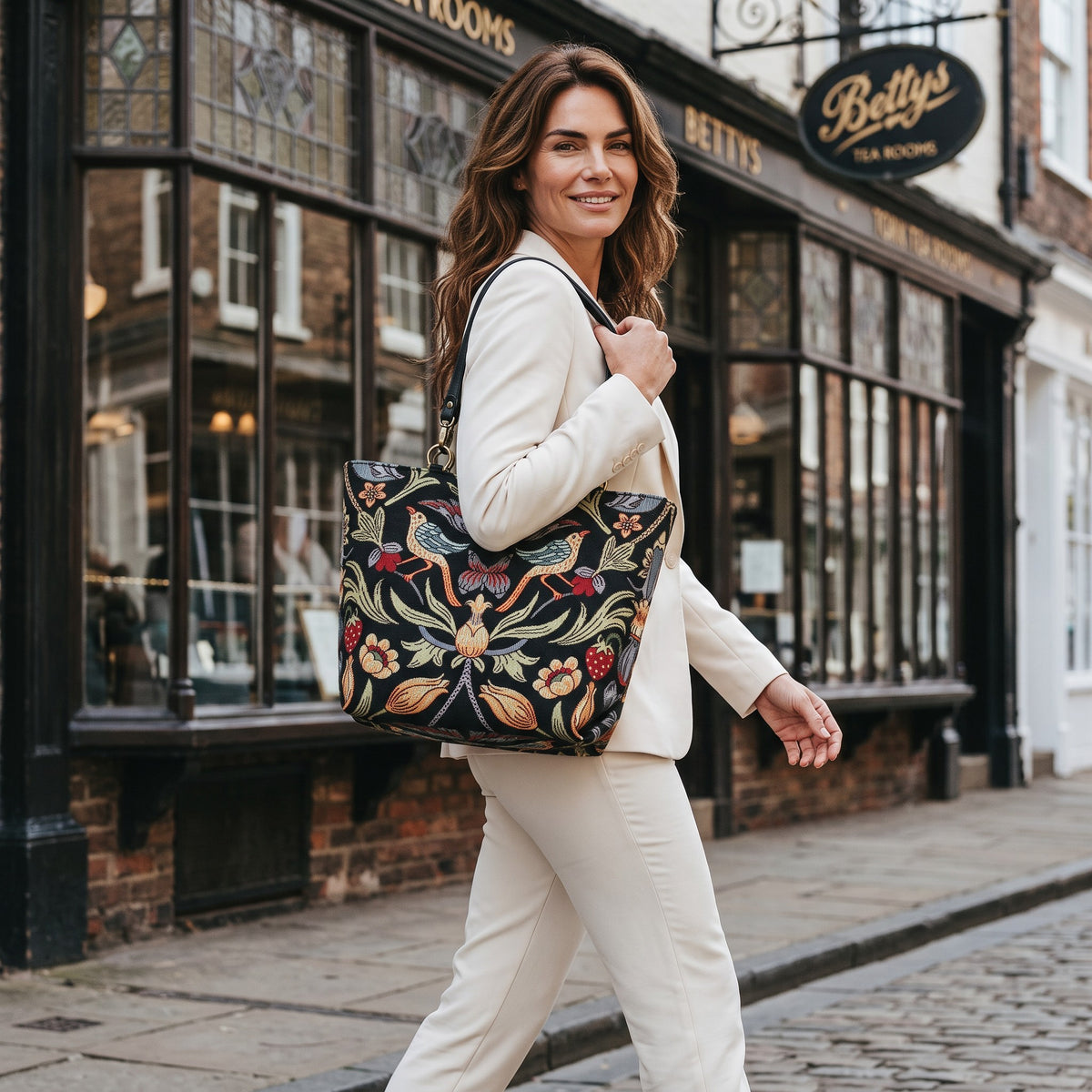 A model walking outside Bettys Tea Rooms in Yorkshire, carrying the William Morris Heritage Shoulder Bag, Genuine Leather Strap by Umpie Handbags