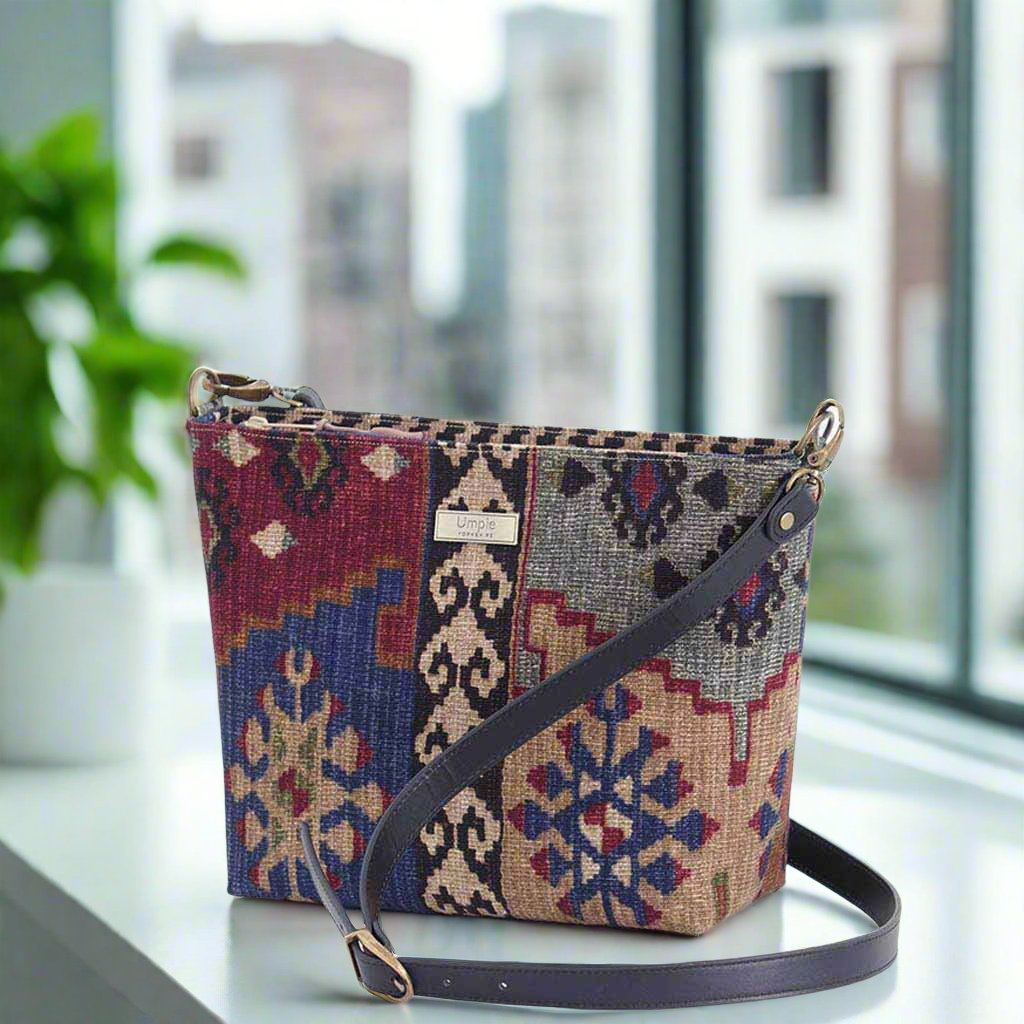 Canvas crossbody bag showcasing intricate Kilim design with traditional diamond motifs, premium black leather strap with brass buckle adjustment, compact structured silhouette - angled view by Umpie Handbags